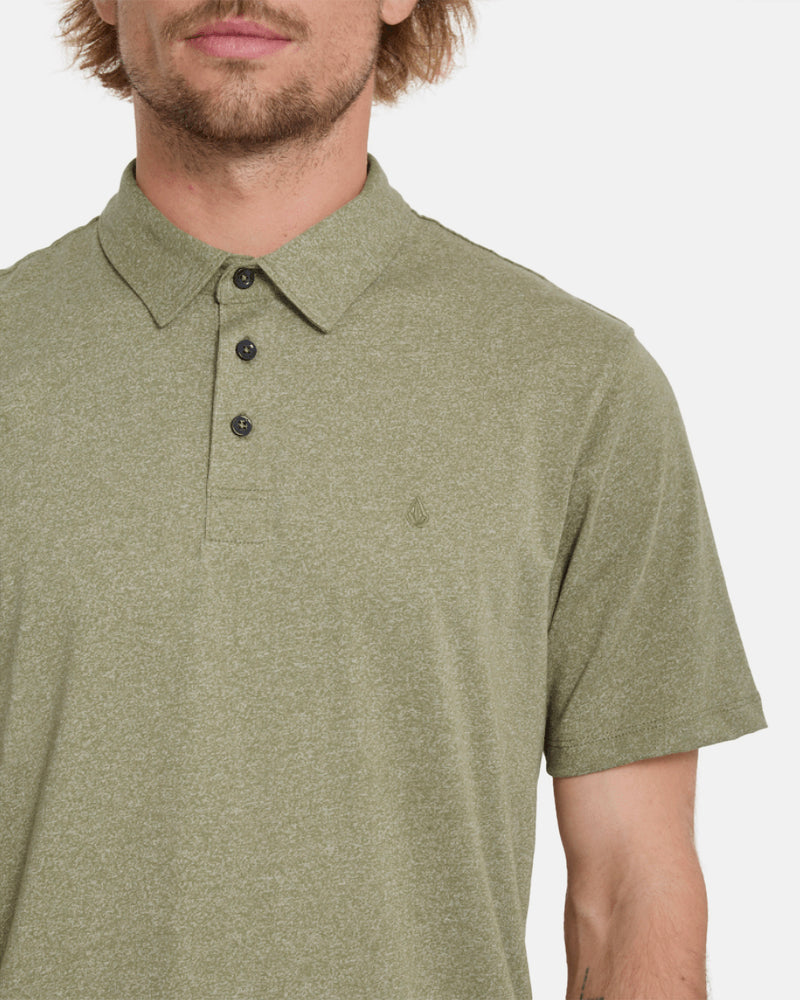 A man with light facial hair wears the Volcom Men's Wowzer Polo Short Sleeve Shirt in light olive green, featuring a soft cotton-poly blend, three buttons, and subtle branding, standing against a plain white background. Only his upper half is visible.