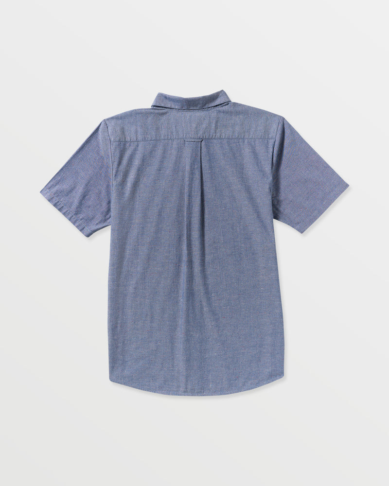 The Men's Date Knight Short Sleeve Shirt by Volcom is a classic-fit blue chambray shirt, shown from the back, with a center pleat and curved hem.