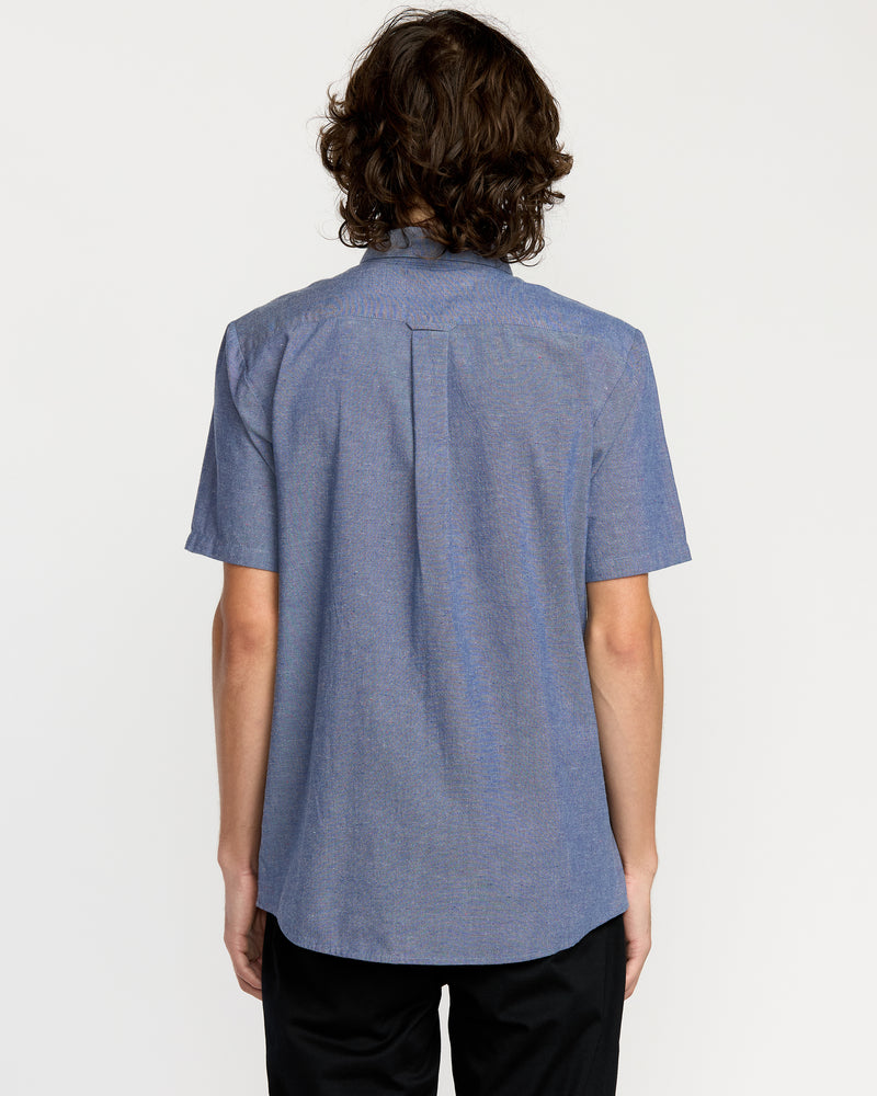 A person with wavy, medium-length brown hair stands with their back to the camera, wearing the Men's Date Knight Short Sleeve Shirt and black pants against a plain white background.