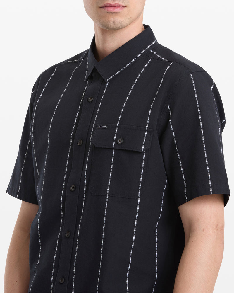 A man models the Volcom Men's Whitworth Short Sleeve shirt in black with white vertical stripes and a chest pocket, shown from shoulders to waist against a white background.