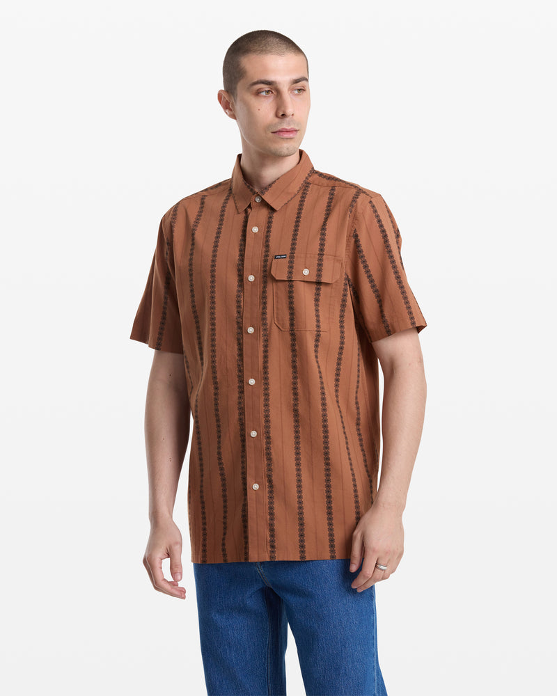 A man with short hair wears the Volcom Men's Whitworth Short Sleeve shirt, featuring vertical jacquard stripes and 100% cotton fabric, with blue jeans, standing against a plain white background.