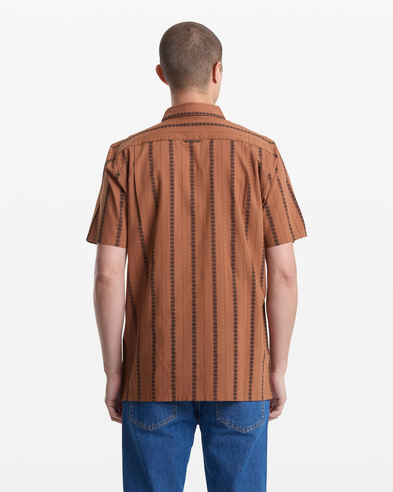 A person with short hair, shown from the back against a white background, is wearing blue jeans and the Volcom Men's Whitworth Short Sleeve—a brown 100% cotton short-sleeve button-up shirt with black jacquard stripes.