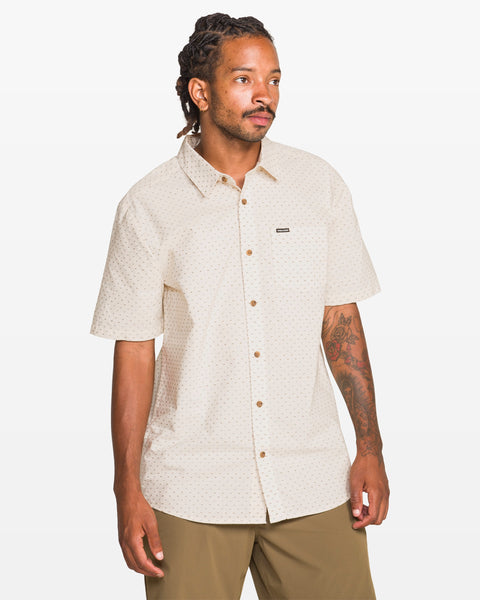 A man with dreadlocks and a tattoo on his left arm wears the Volcom Men's Bankstone II Short Sleeve Tee and khaki pants, standing against a plain white background.