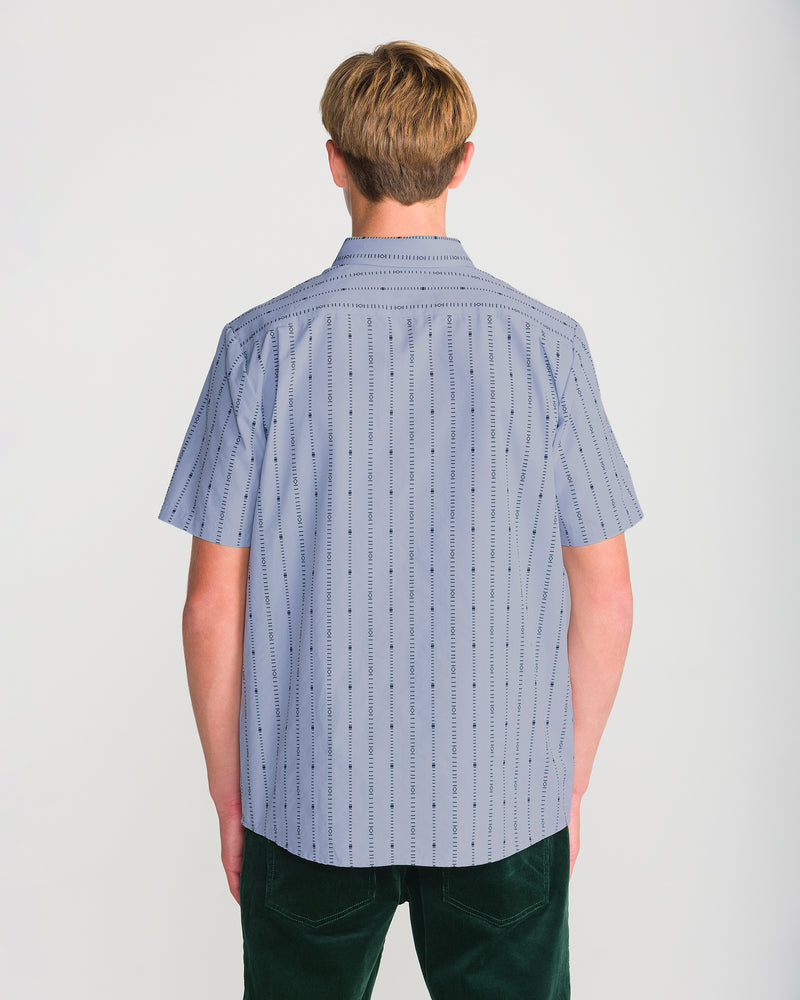 Back view of a person wearing a Volcom Men’s Bankstone Short Sleeve, a pale blue, short-sleeve button-up shirt with a pattern of vertical dashed lines and small dark shapes.