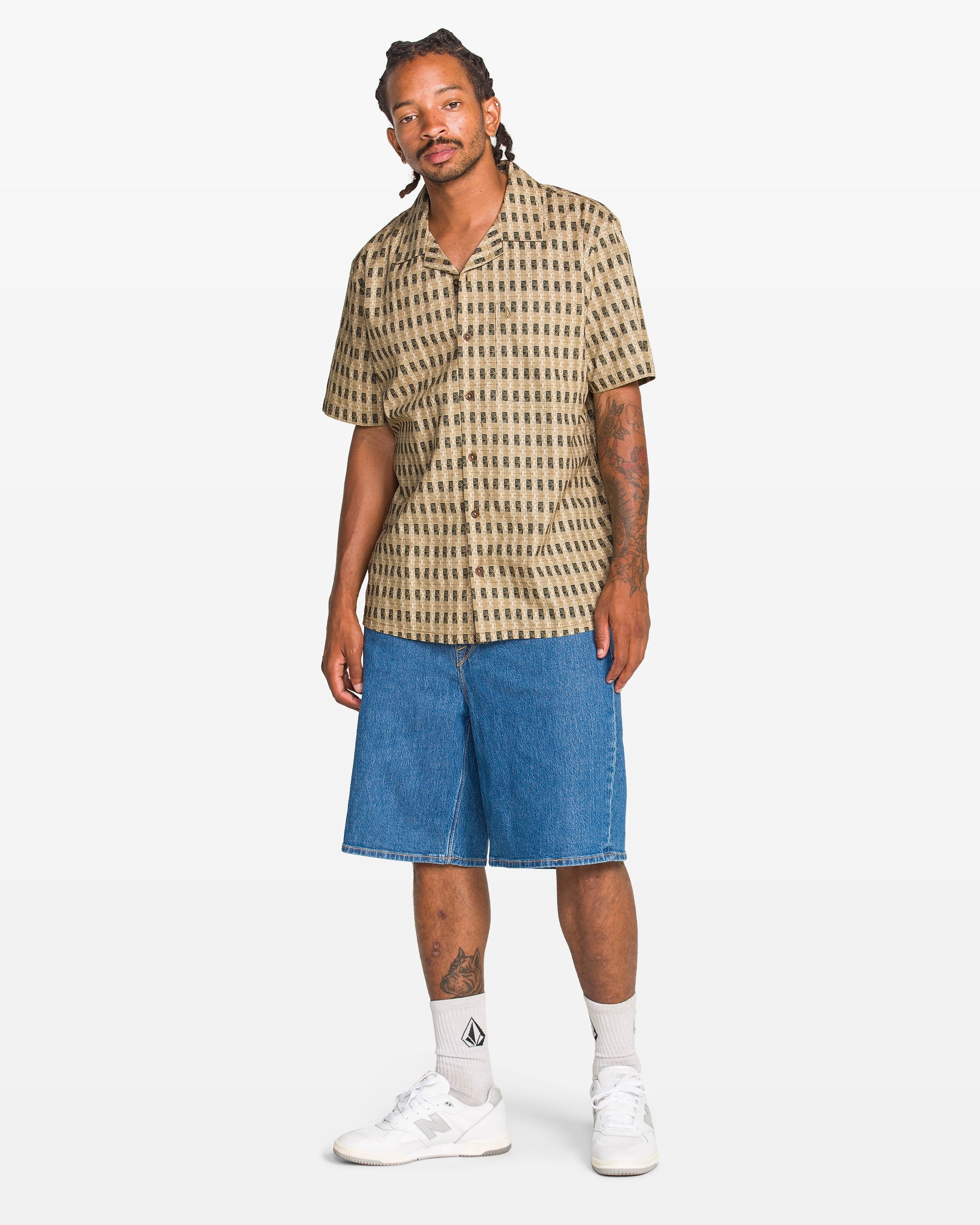 Man wearing a patterned shirt and denim shorts on a white background