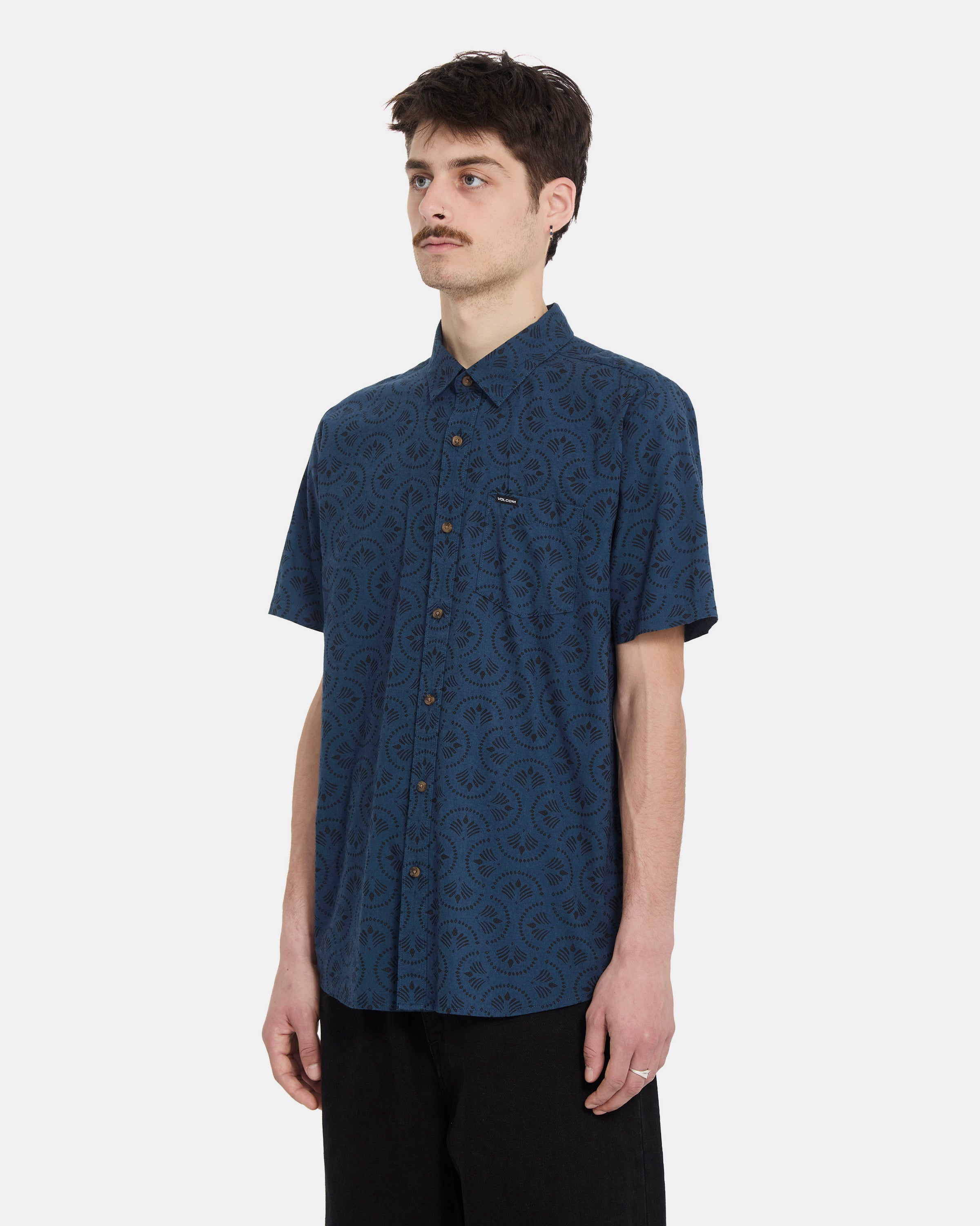 A man with short brown hair and a mustache wears the Volcom Men's Scaler Stone Woven Short Sleeve Shirt in midnight blue against a plain white background.
