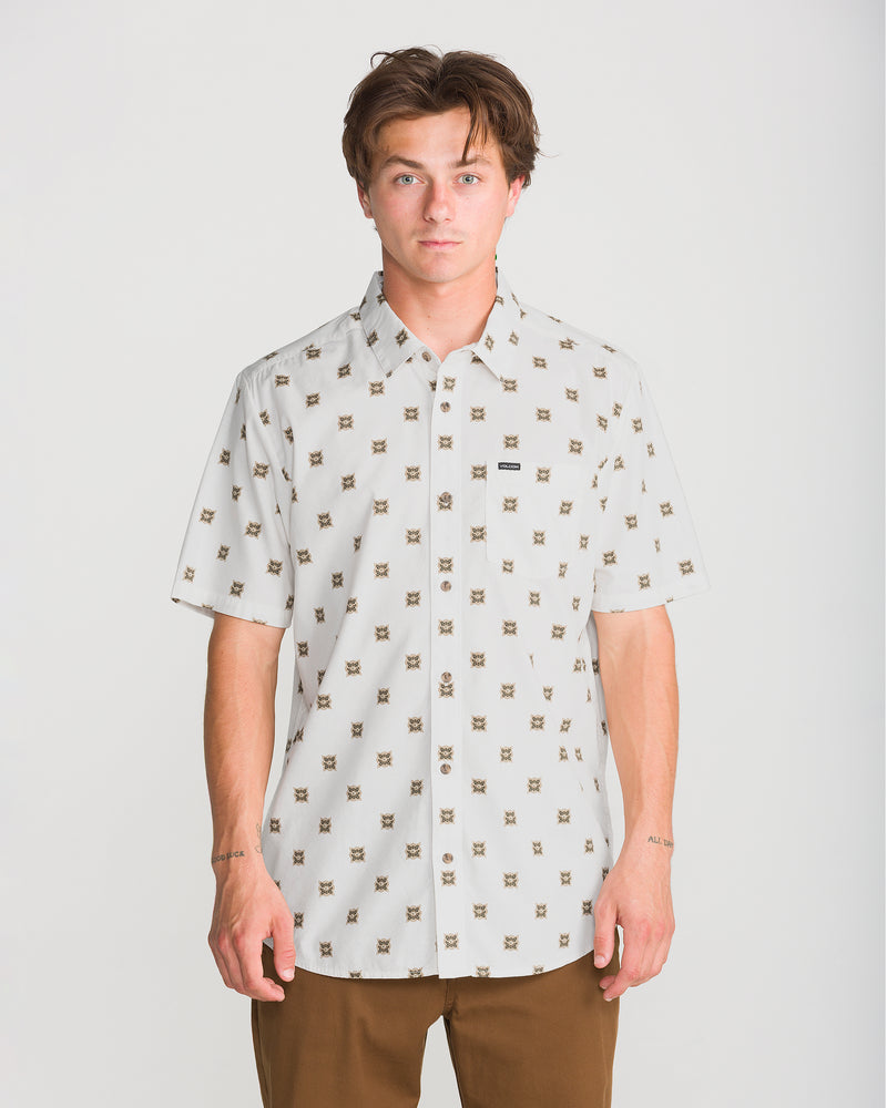 A person wearing a Volcom Men’s Scaler Stone Short Sleeve, an off-white, classic fit button-down shirt with short sleeves and a repeating small geometric pattern.
