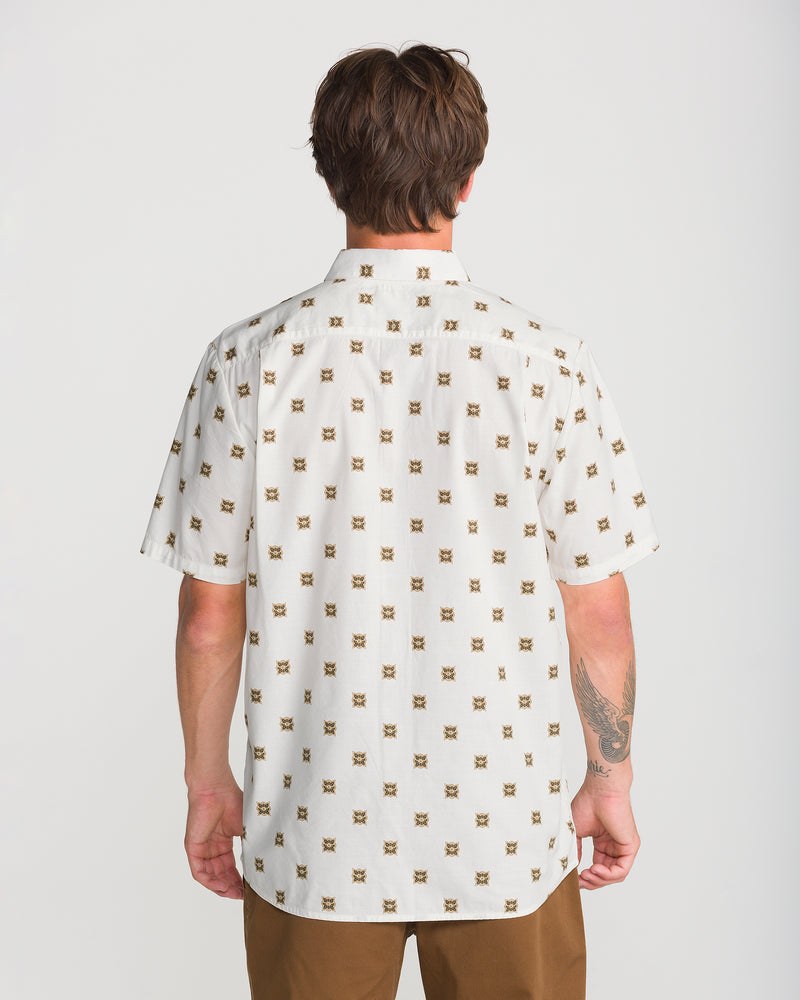 Back view of a person wearing a Men’s Scaler Stone Short Sleeve in an off-white classic fit with a brown geometric allover print, paired with brown pants.