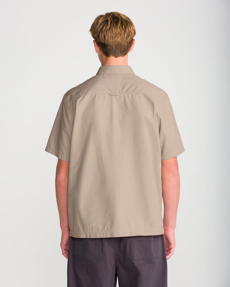 A person viewed from the back wearing a sturdy plain-weave tan short-sleeved Men’s Driggs Workwear Short Sleeve button-up shirt and dark grey shorts.