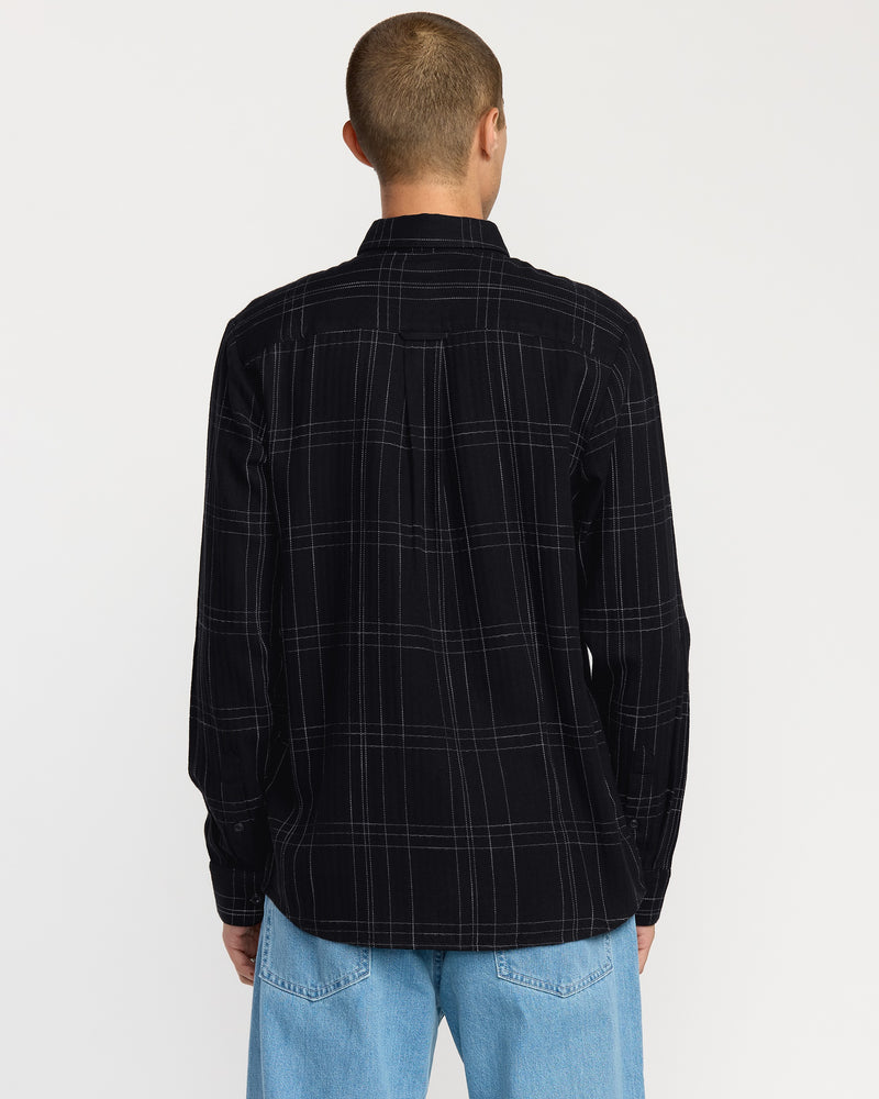 A person with short hair stands with their back to the camera, wearing the Volcom Men's Date Knight Long Sleeve Shirt in black plaid and light blue jeans against a plain white background.