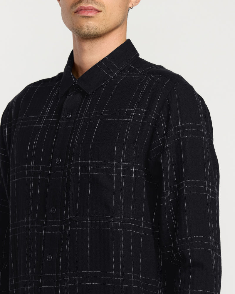A man wears the Volcom Men's Date Knight Long Sleeve Shirt—a classic-fit black button-up with a subtle white plaid pattern, made from premium cotton blend—shown chest up against a plain backdrop.