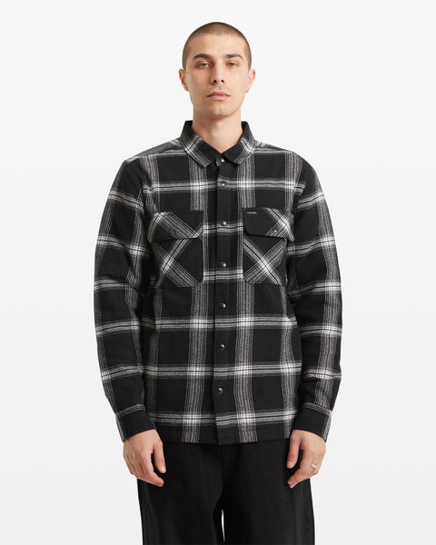 A person with short hair wears the Volcom Men's Wilderstone Long Sleeve shirt in classic black and white cotton with two chest pockets, standing against a plain white background.
