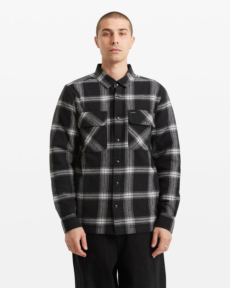 A person with short hair wears the Volcom Men's Wilderstone Long Sleeve shirt in classic black and white cotton with two chest pockets, standing against a plain white background.