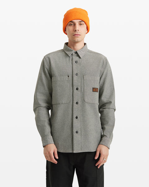 A person wearing the Men's Levelstone Long Sleeve Shirt in grey with two chest pockets and an orange knit beanie, standing against a plain white background.