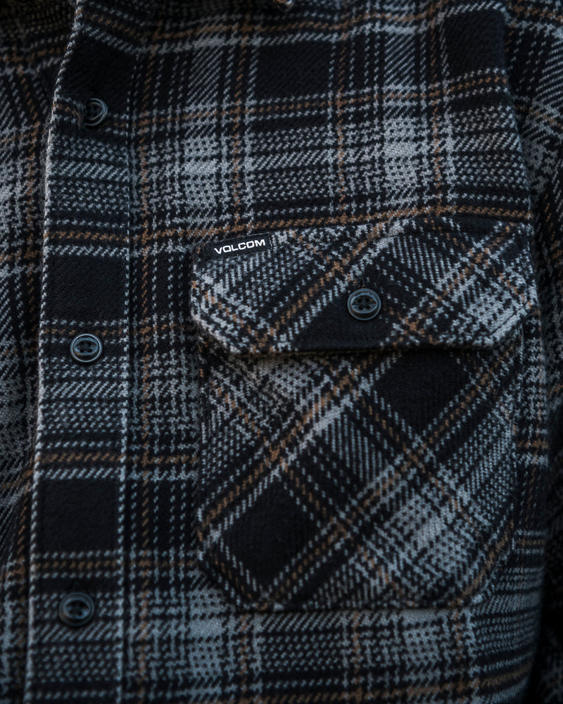 A close-up of the Volcom Men’s Johnstone Long Sleeve Shirt, a black, gray, and brown plaid heavyweight flannel featuring a buttoned chest pocket with a small Volcom woven label above it.