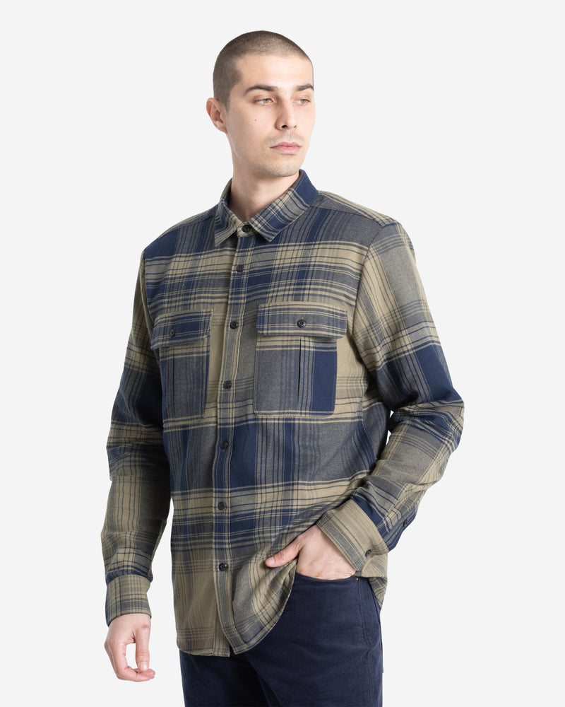 A man models the Volcom Men's Parkstone Long Sleeve Shirt—a blue and beige button-up plaid—standing with one hand in his pocket and looking to the side against a plain white background.