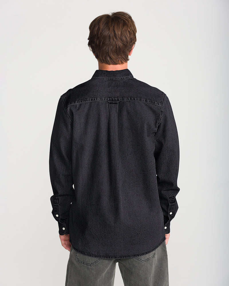 Back view of a person wearing a black, relaxed-fit, long-sleeve Volcom Men’s Goodwin Long Sleeve button-up denim shirt.