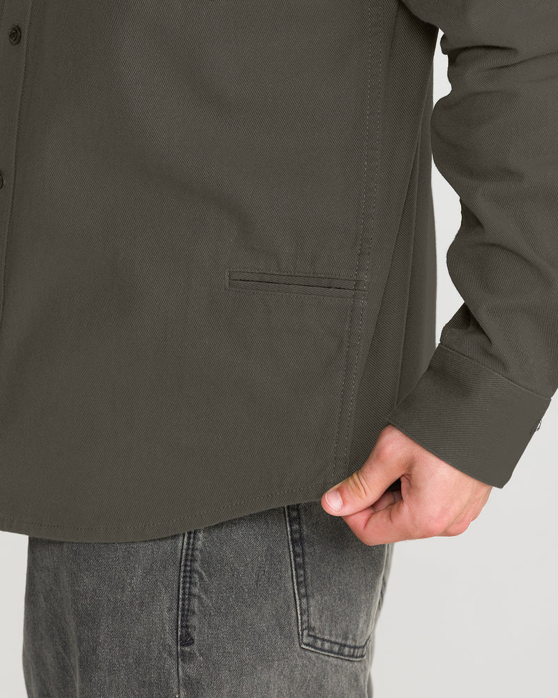 Close-up of a Men’s Stockholm Long Sleeve in olive green cotton twill with a relaxed fit and a single welt pocket on the front.