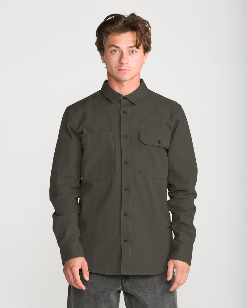 A man wearing a Volcom Men’s Stockholm Long Sleeve, a relaxed fit, dark olive green long-sleeve cotton twill overshirt with two chest pockets.