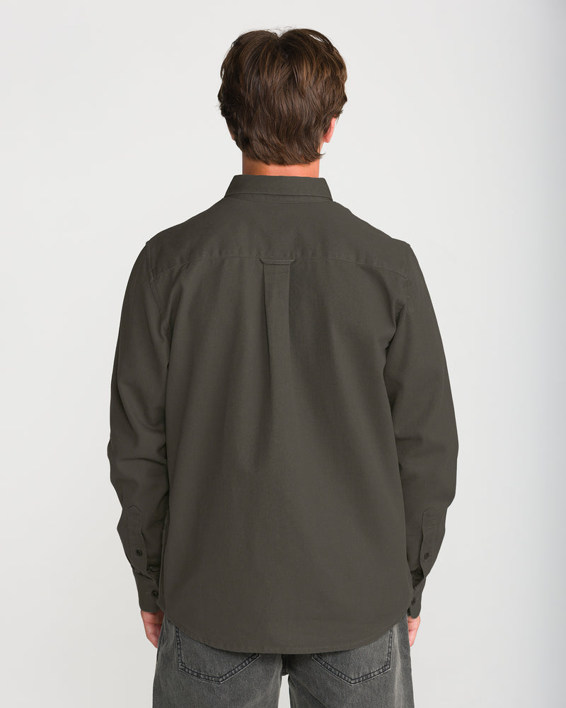 Back view of a person wearing a relaxed fit, dark olive green cotton twill Volcom Men’s Stockholm Long Sleeve overshirt and dark gray jeans.