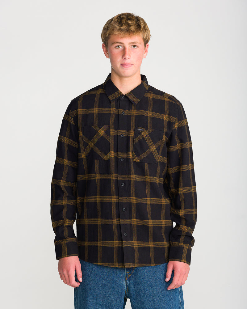 A person wearing a Volcom Men’s Netastone Long Sleeve classic-fit, yarn-dyed flannel shirt in Antique Black with two chest pockets and blue jeans.