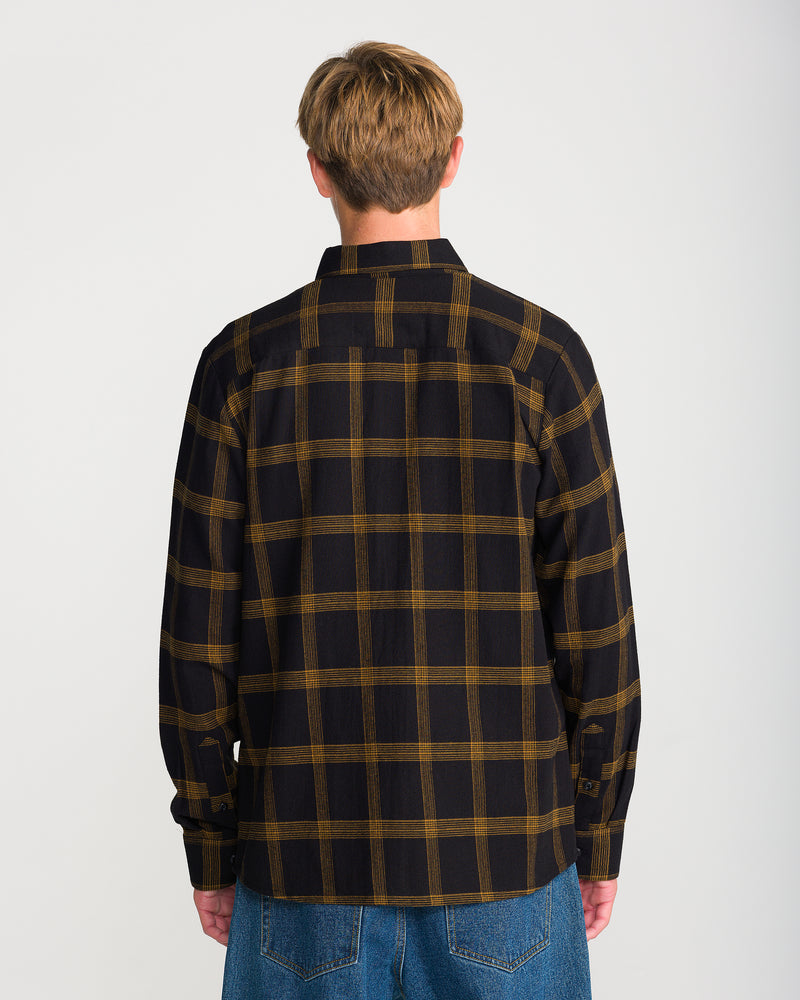 A person seen from behind wearing a Volcom Men’s Netastone Long Sleeve Antique Black yarn-dyed flannel button-down shirt and blue jeans.