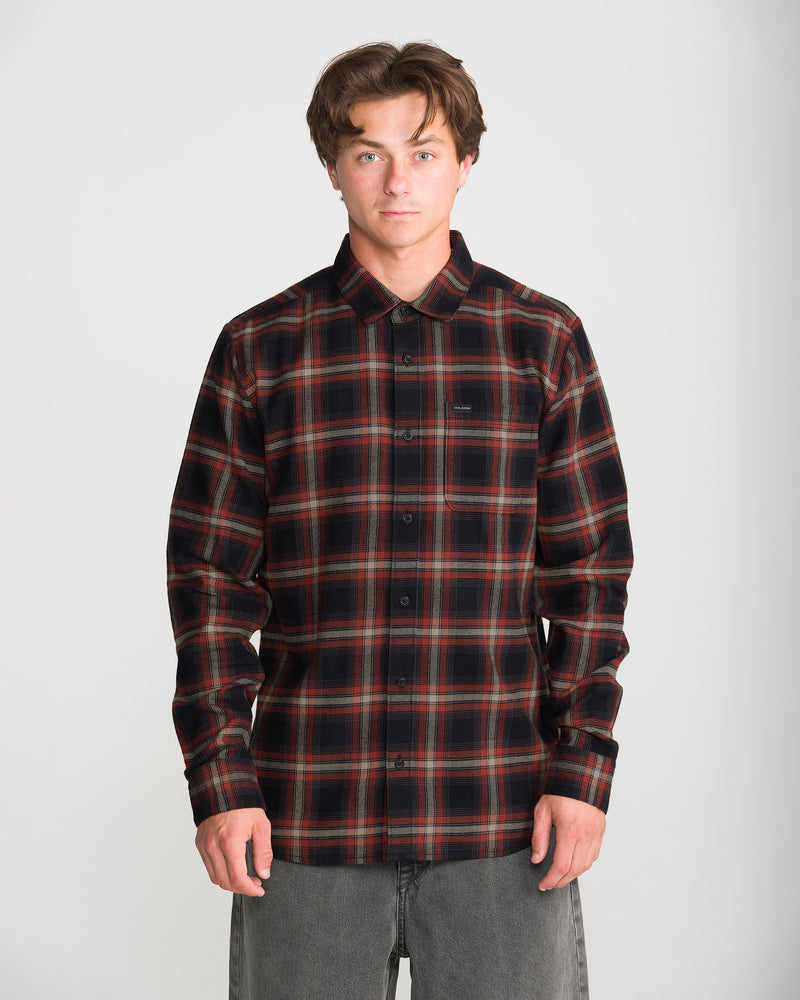 A man wearing a black and red long-sleeve plaid Volcom Men’s Caden Plaid Long Sleeve flannel shirt in a classic fit.