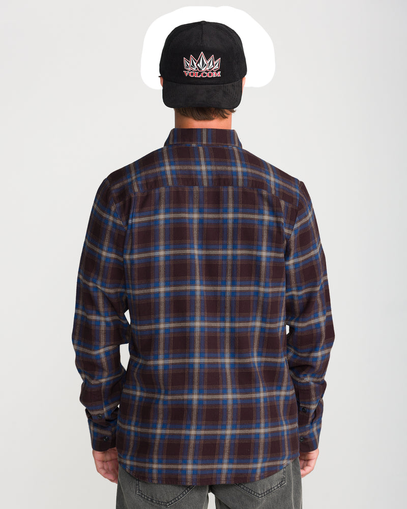 A man seen from behind wearing a brown and blue Volcom Men’s Caden Plaid Long Sleeve cotton shirt and a black baseball cap.