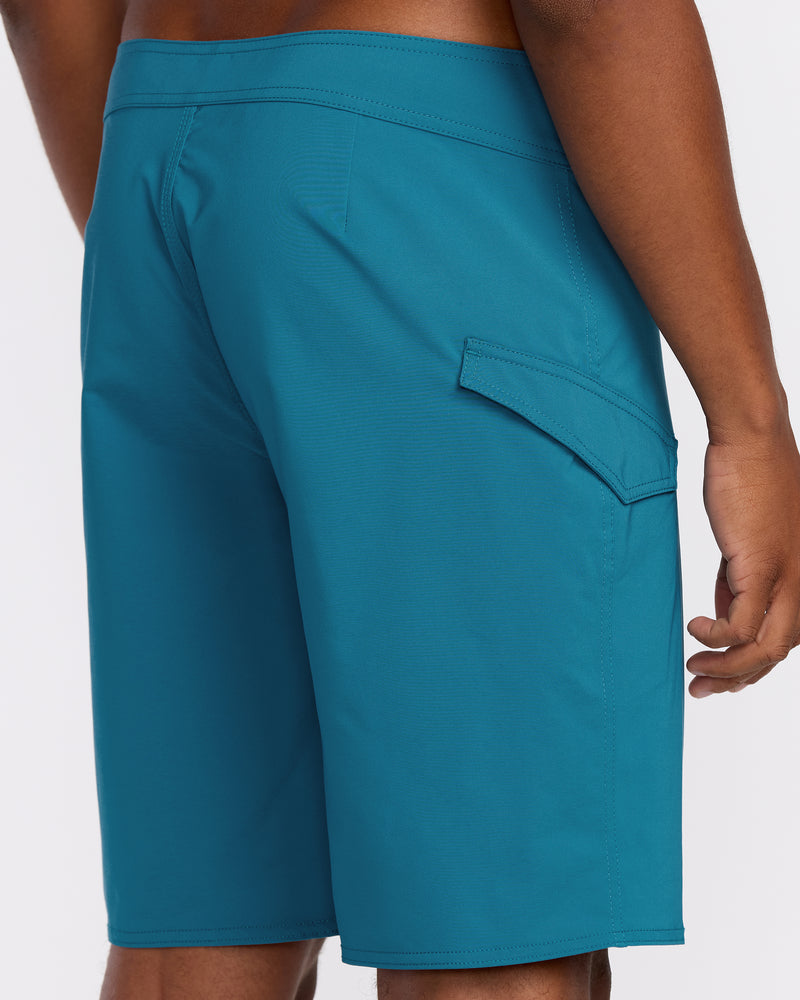 A person wearing Men's Lido Solid Mod Trunks in teal, knee-length with a side flap pocket, photographed from the back against a plain white background.