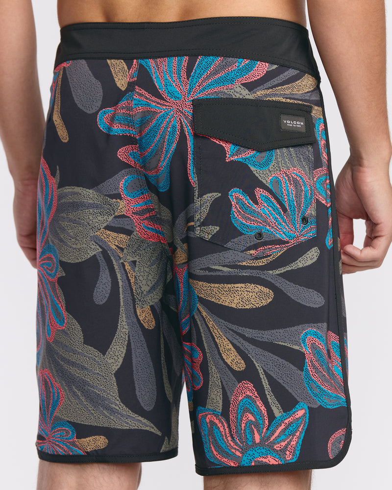 A person is wearing Men's Infuse Scallop Mod Trunks by Volcom—black board shorts with a red, blue, and tan floral pattern. Shown from the back waist to knees, these quick-drying trunks have a back pocket with a black flap and small logo.