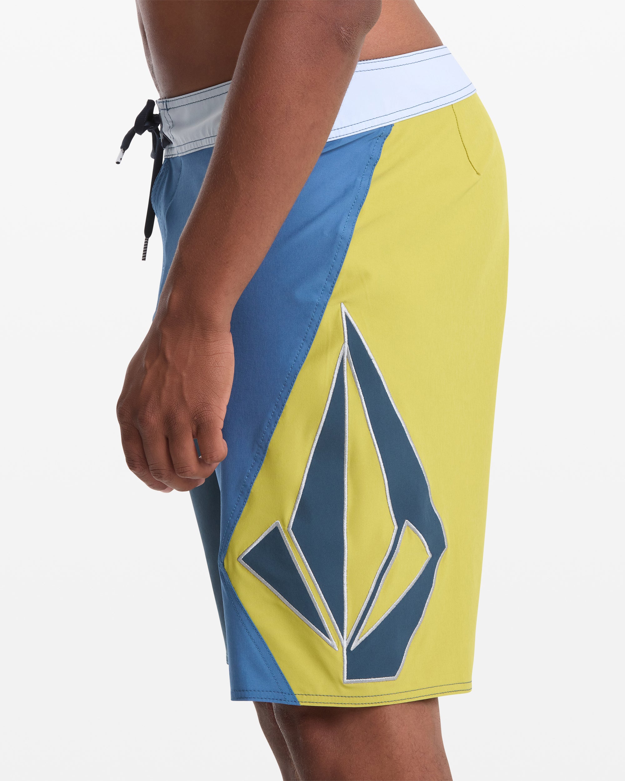 A person wearing Volcom Men's Foster Mod 21 board shorts, featuring a large geometric logo on the side, is photographed from the hip down against a plain white background.