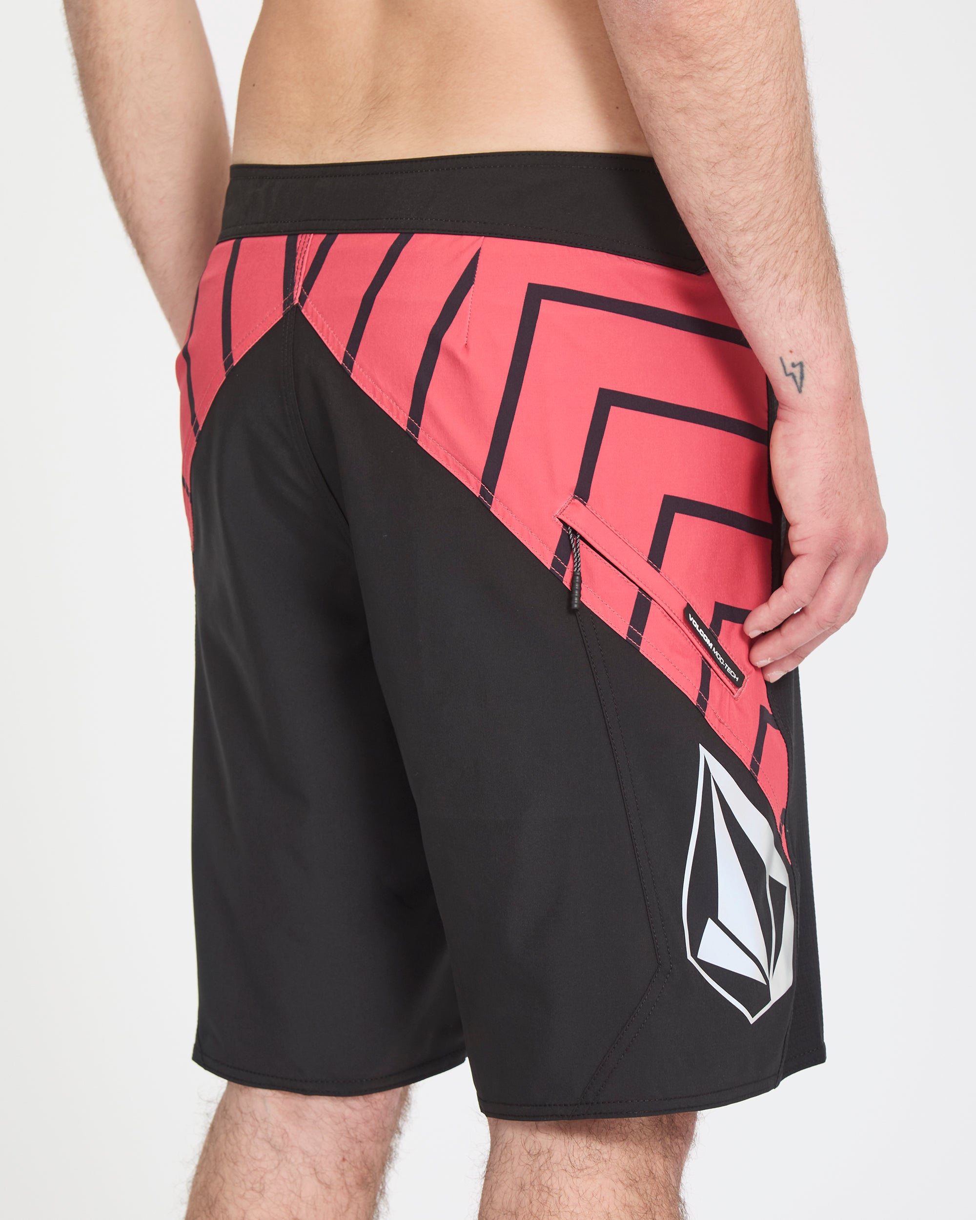 A person is shown from the back wearing Volcom Men's Ripper Mod 21 board shorts in black and red with a large white Volcom logo on the side, their right hand resting by their side.