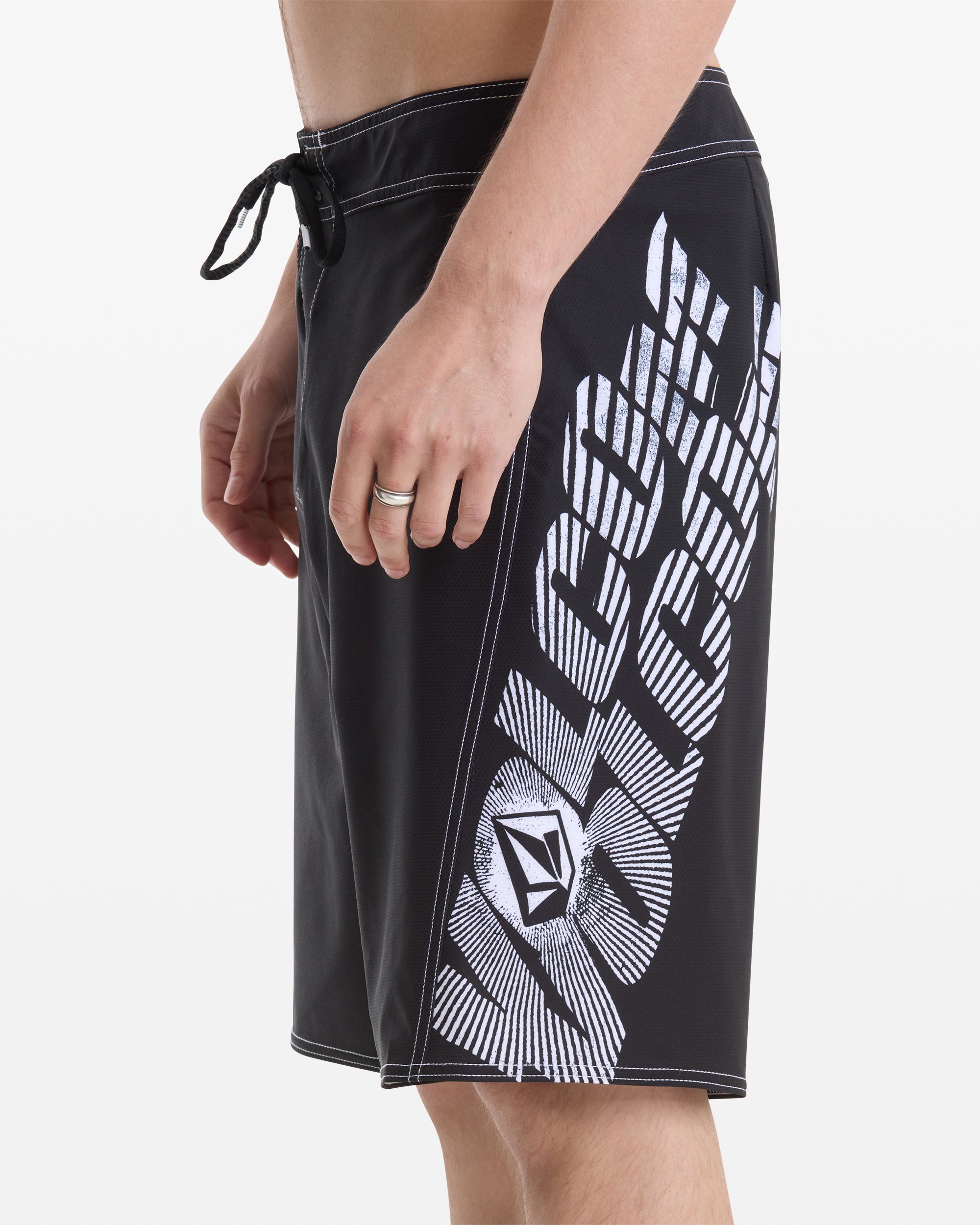A man wears Volcom Men's Reaper Mod 21 black board shorts with a white logo and graphic on the side, shown waist to knee against a plain white background.