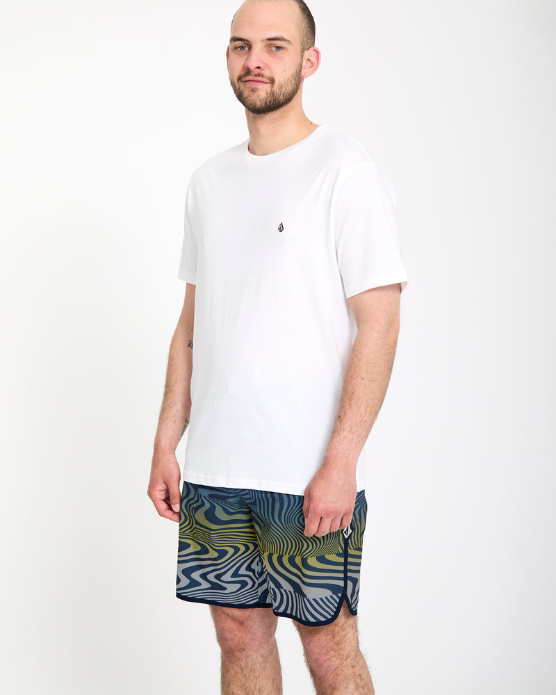 A man wears Volcom's Men's Encounter Scallop Mod 19 shorts and a white shirt.