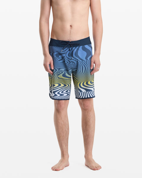 A person stands barefoot in Volcom’s Men's Encounter Scallop Mod 19 board shorts featuring blue, yellow, white, and black wavy patterns plus a dark drawstring waistband. The background is plain white.
