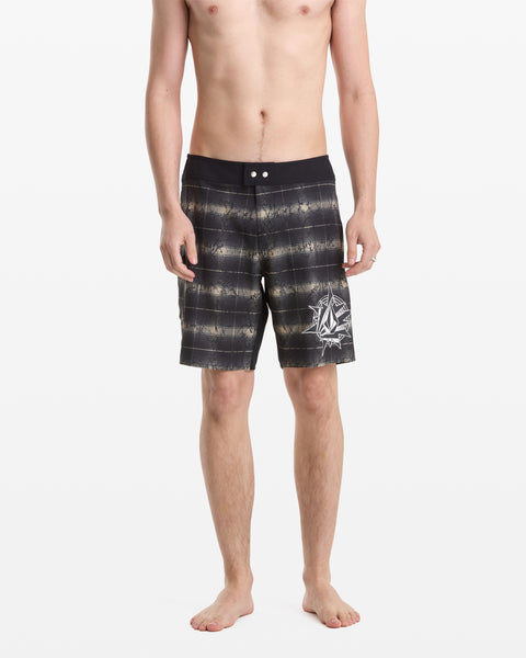 A shirtless man stands barefoot against a white background wearing Volcom Men’s Grunge Snap Mod 18 board shorts, featuring black and gray stripes and a white abstract graphic on the left leg.