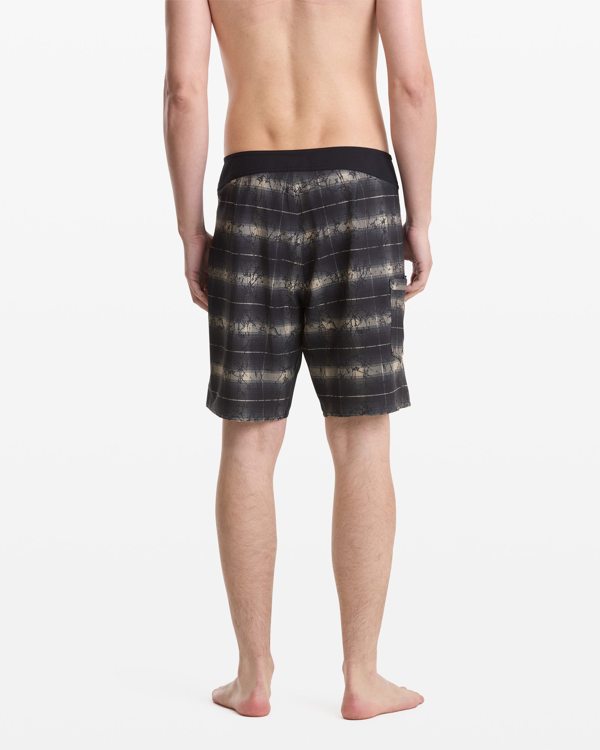 A shirtless person is standing barefoot, facing away from the camera, wearing Volcom Men's Grunge Snap Mod 18 shorts with a black waistband and black and beige pattern. The background is plain white.