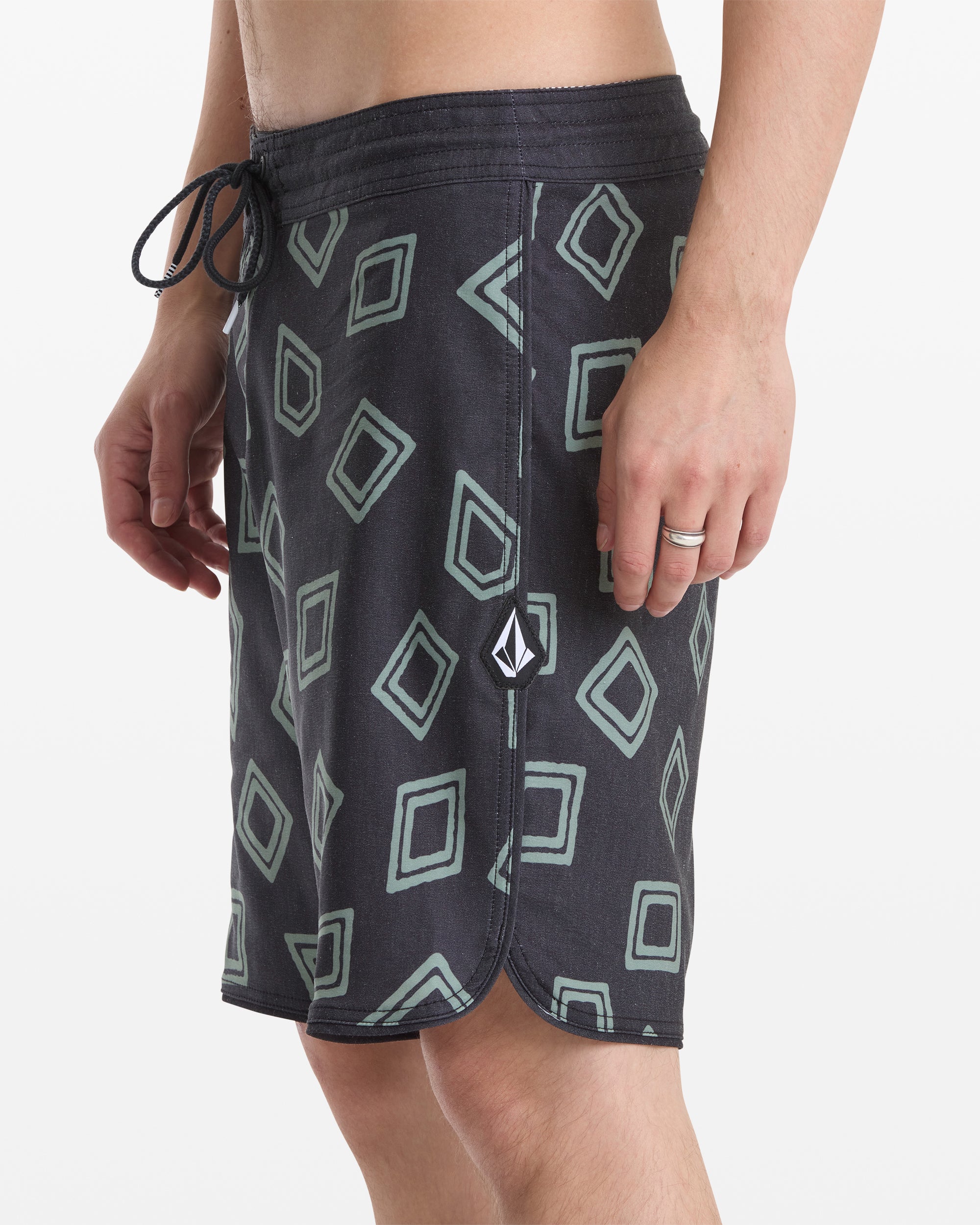 A person wearing Volcom Men's Contact Scallop Stoney 19 swim shorts with a light geometric diamond pattern, drawstring waistband, and small logo patch near the hem; only lower torso and upper legs are visible.