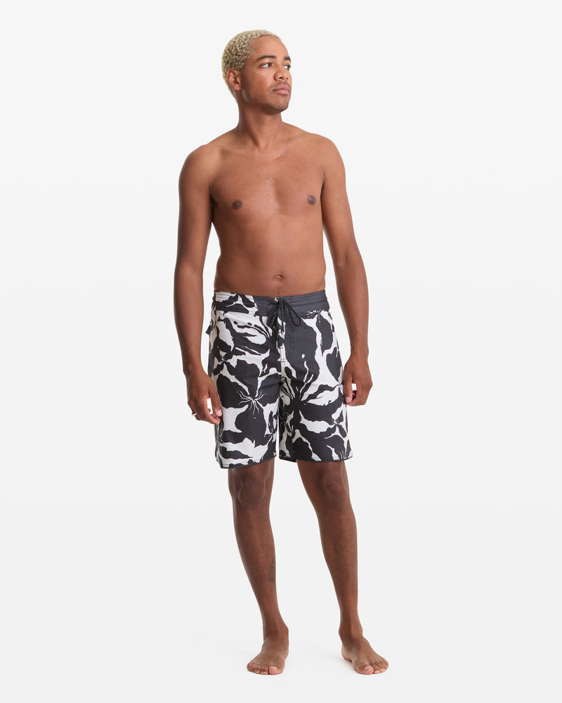 A shirtless man with short blond hair stands barefoot against a white background, modeling the Volcom Men's Contact Scallop Stoney 19 swim trunks. He looks slightly to the side with a relaxed posture.