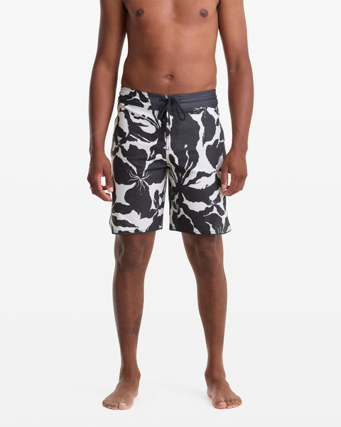A man stands barefoot against a white background, wearing Volcom Men's Contact Scallop Stoney 19 swim trunks with a black and white camouflage pattern and drawstring waist. He is shirtless, arms relaxed at his sides.