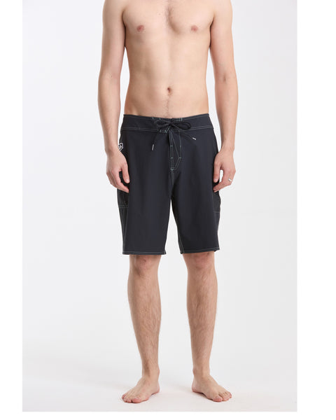 A barefoot person stands facing forward, wearing Volcom Men's Povj Redeemer Mod black knee-length nylon boardshorts featuring Cinch Fly and 4-way stretch. The background is plain white.
