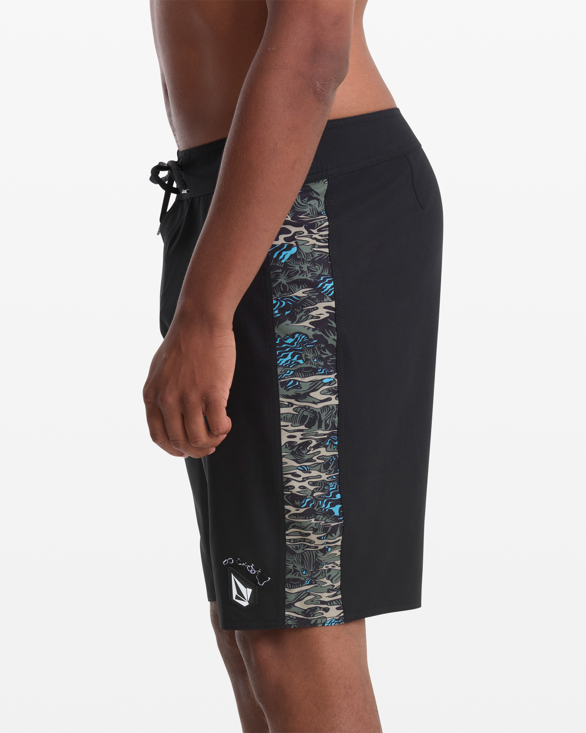 A man models the Volcom Men's Parillo Mod 21 board shorts, featuring black fabric with a blue and grey camo side panel, a drawstring waist, and a small white logo near the hem. Side view with visible torso.
