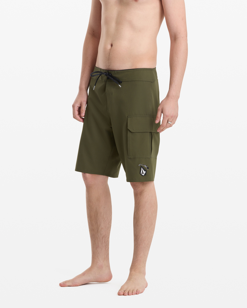 A man stands barefoot in Volcom Men's Hawaii Truly Preemo Mod 20 olive green board shorts with a drawstring waist and side cargo pocket, shown against a plain white background.