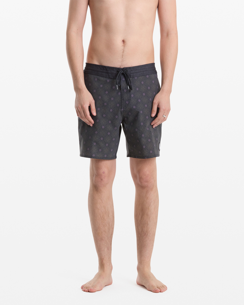 A man stands against a plain white background wearing Volcom Men's Psyche Cotton Stoney 17 board shorts featuring a subtle pattern; he is shirtless and barefoot.
