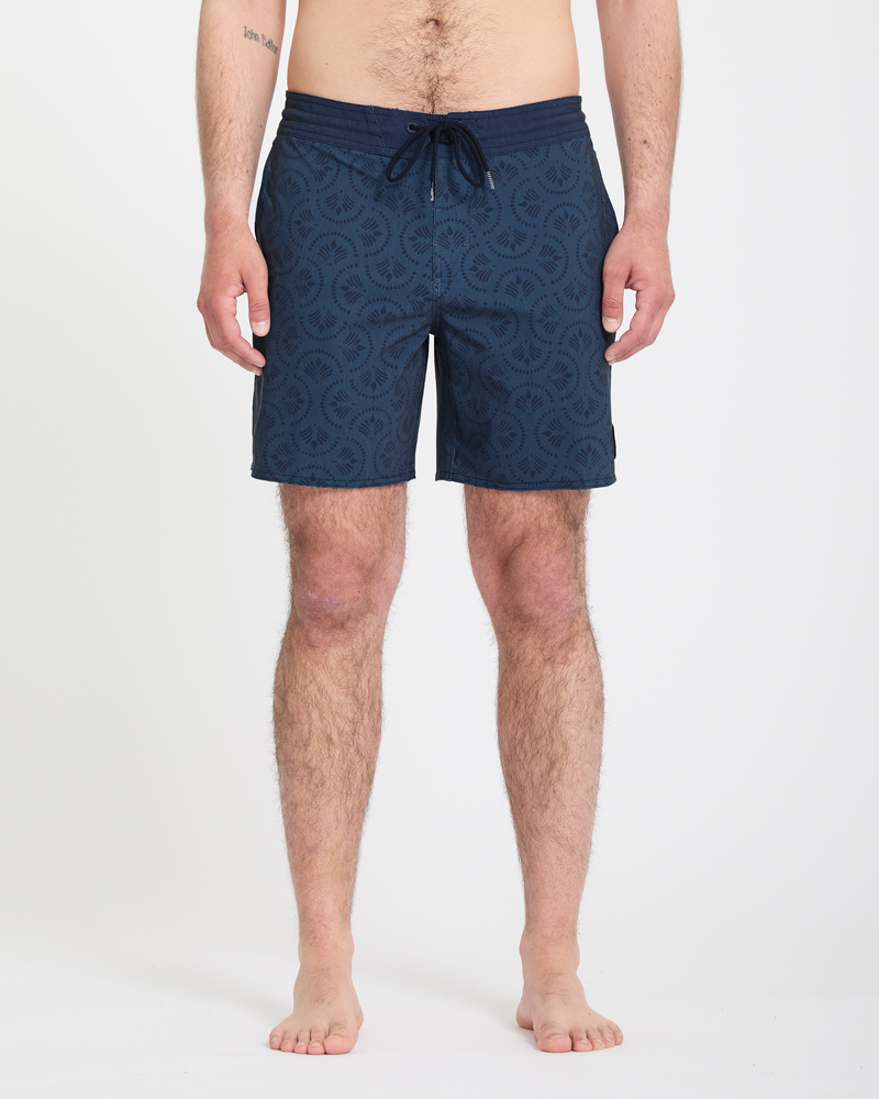 A man stands barefoot against a white background, wearing Volcom Men's Psyche Cotton Stoney 17 navy swim trunks with a drawstring waist. His arms rest at his sides, and only his lower body is fully visible.