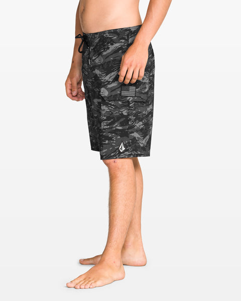 A person stands barefoot in profile wearing Volcom Men's 4th Of July Preemo Mod boardshorts with Cinch Fly Technology, a side pocket, and a small white logo near the hem, set against a plain white background.