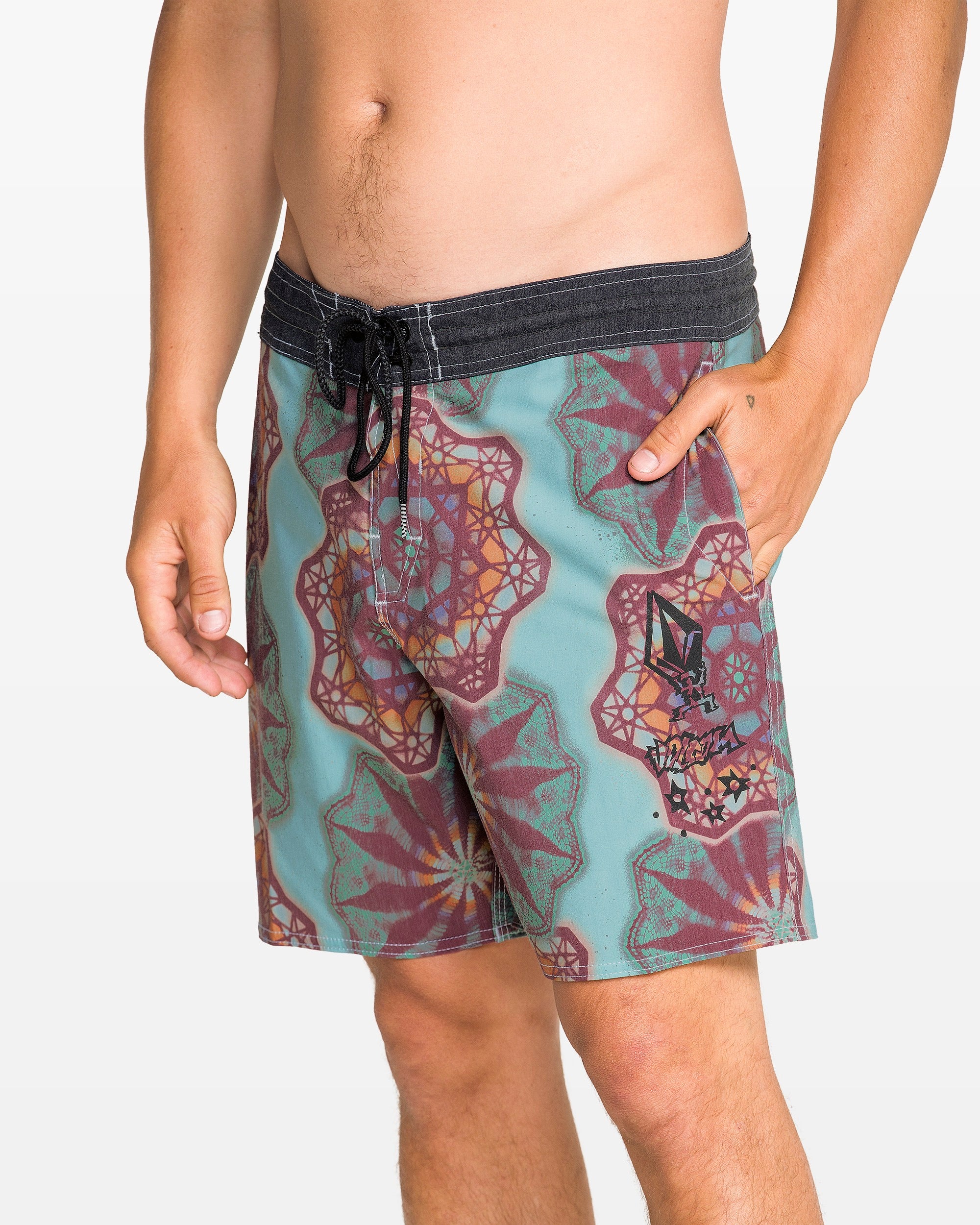 A man wearing Volcom Men's Star Shields Featured Artist Pcs Stoney trunks with a drawstring, one hand in the pocket, stands against a plain white backdrop—bold aquatic style from the Featured Artist Series.