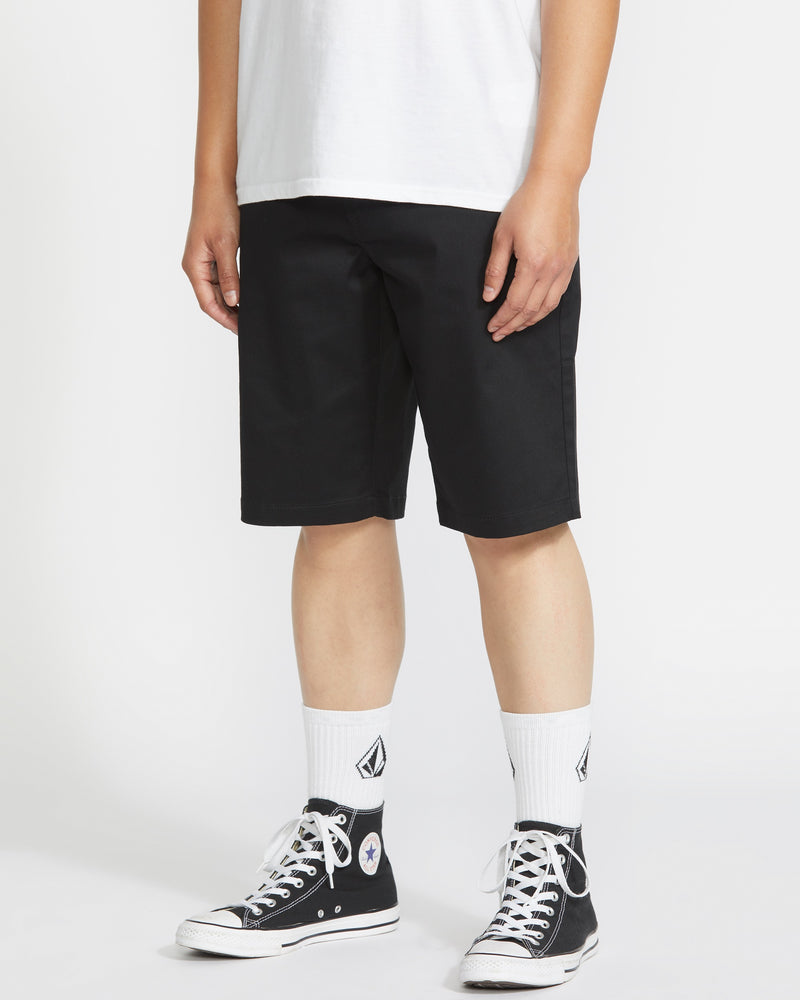 A person wearing a white t-shirt, Volcom Men's Frickin Modern Stretch Shorts, white crew socks with a logo, and black high-top Converse sneakers stands against a plain white background.