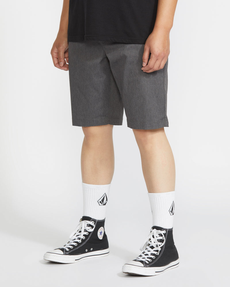 A person in a black t-shirt, Volcom Men's Frickin Modern Stretch Shorts in gray, white crew socks with a black diamond logo, and black high-top Converse sneakers stands against a plain white background.