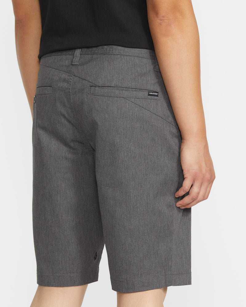 A person in a black shirt and Volcom Men's Frickin Modern Stretch Shorts stands facing away, highlighting the shorts' breathable fabric, two back pockets, and a small Volcom tag above the right pocket.